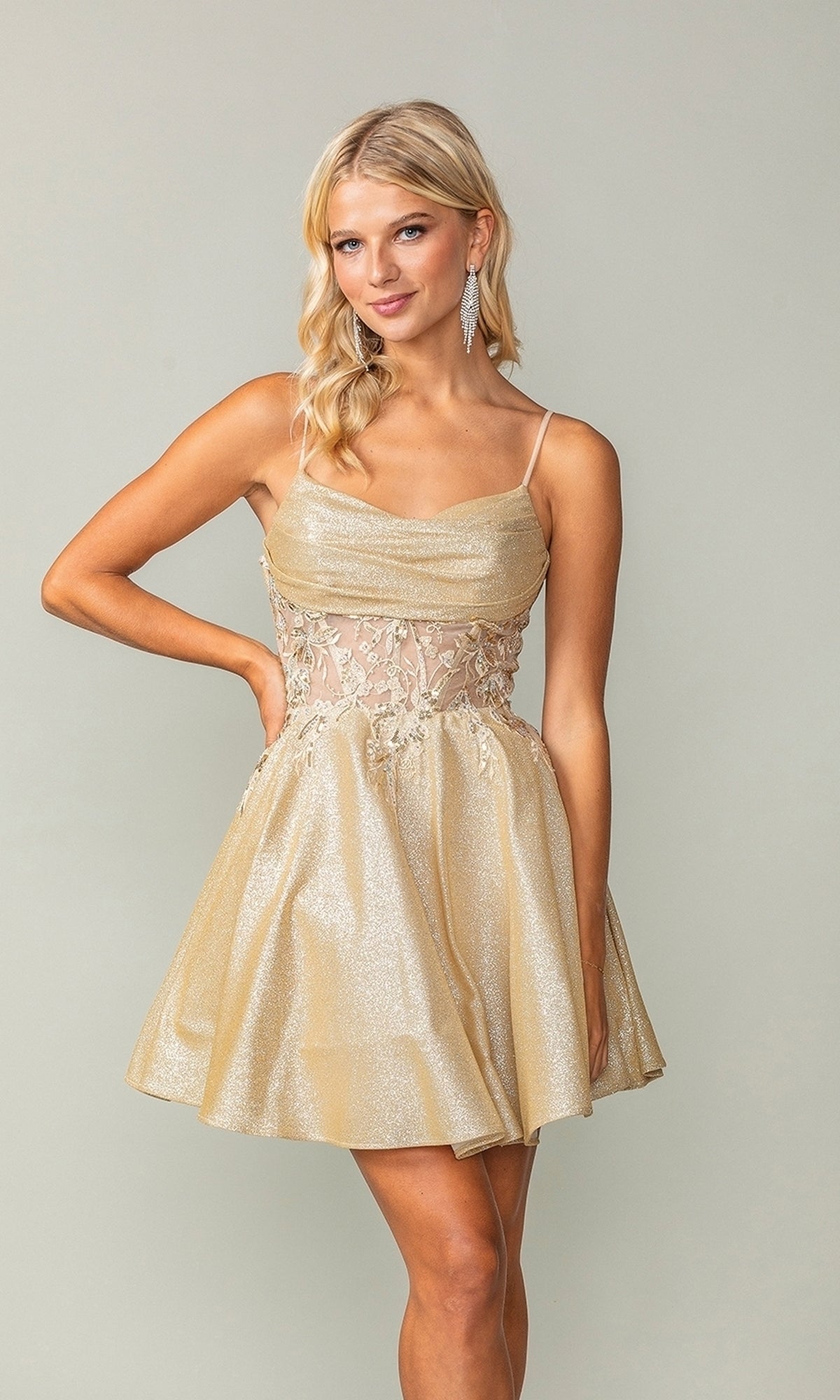 A woman poses in the Cowl-Neck Short Glitter Homecoming Dress 3386, a sleeveless gold party dress featuring sheer embroidered waist detailing, against a plain background.